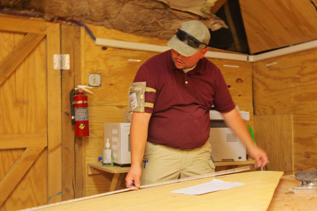 a man cutting plywood and measuring it to make diy cornhole game